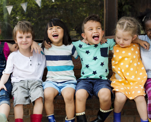 Kindergarten kids friends with arms around each other, sitting and smiling